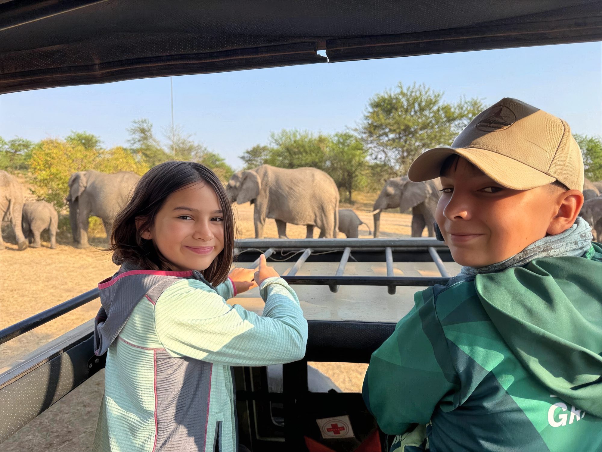 Zwei Kinder im Safarifahrzeug, im Hintergrund eine Elefantenherde