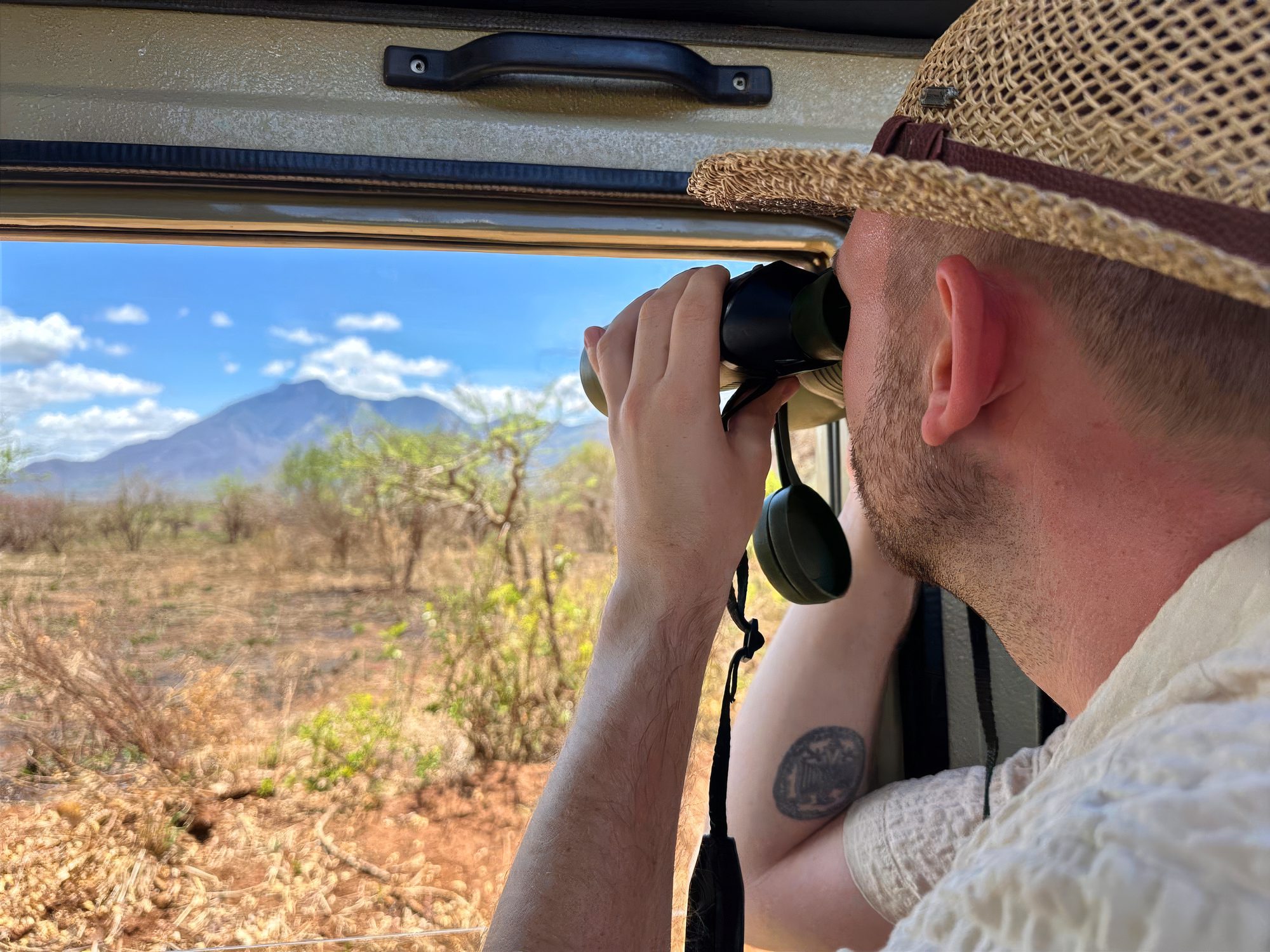 Viajero observando con prismáticos desde el vehículo de safari, con una montaña al fondo