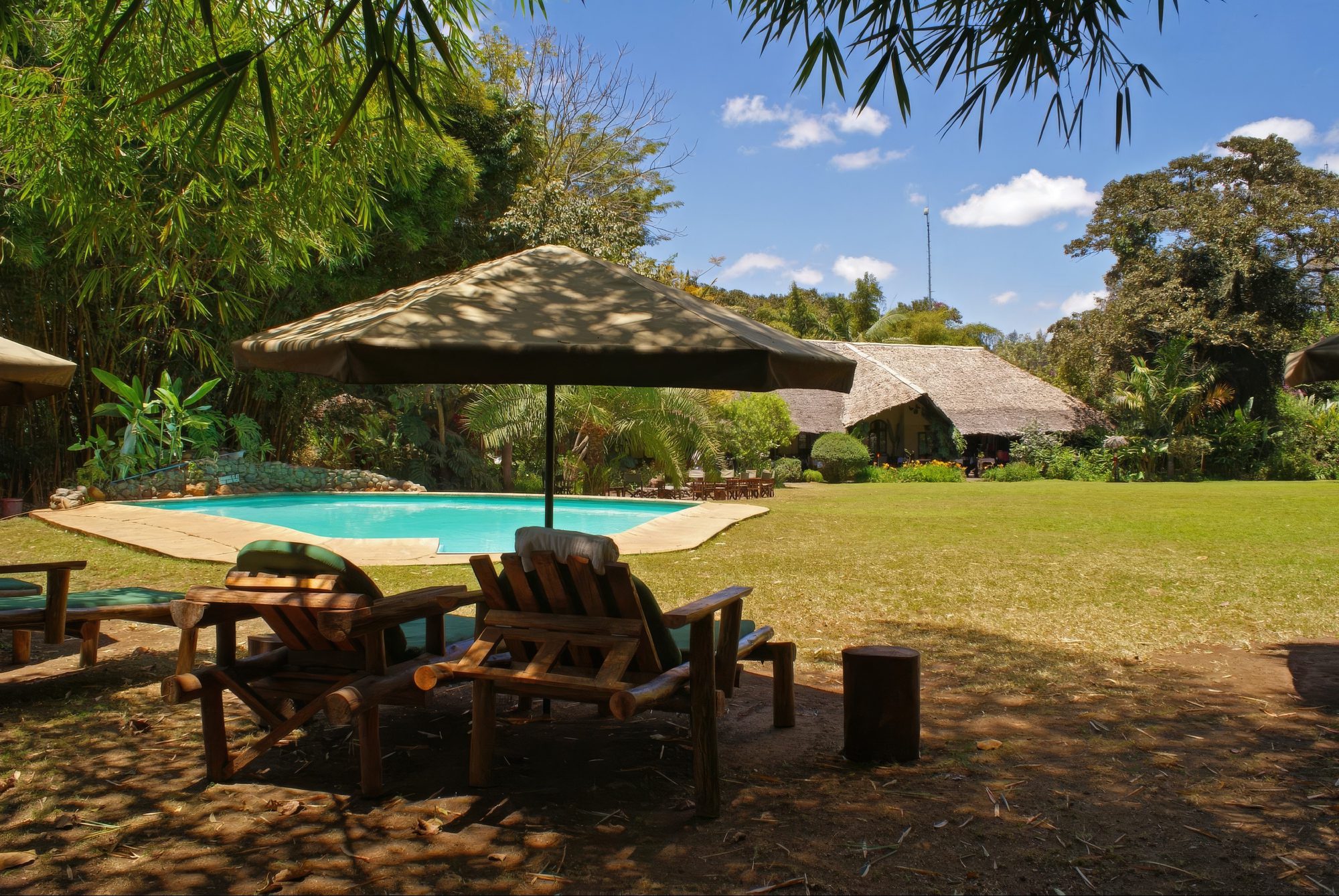 Garten der Moivaro Lodge mit Pool, Sonnenschirm und Rasenfläche
