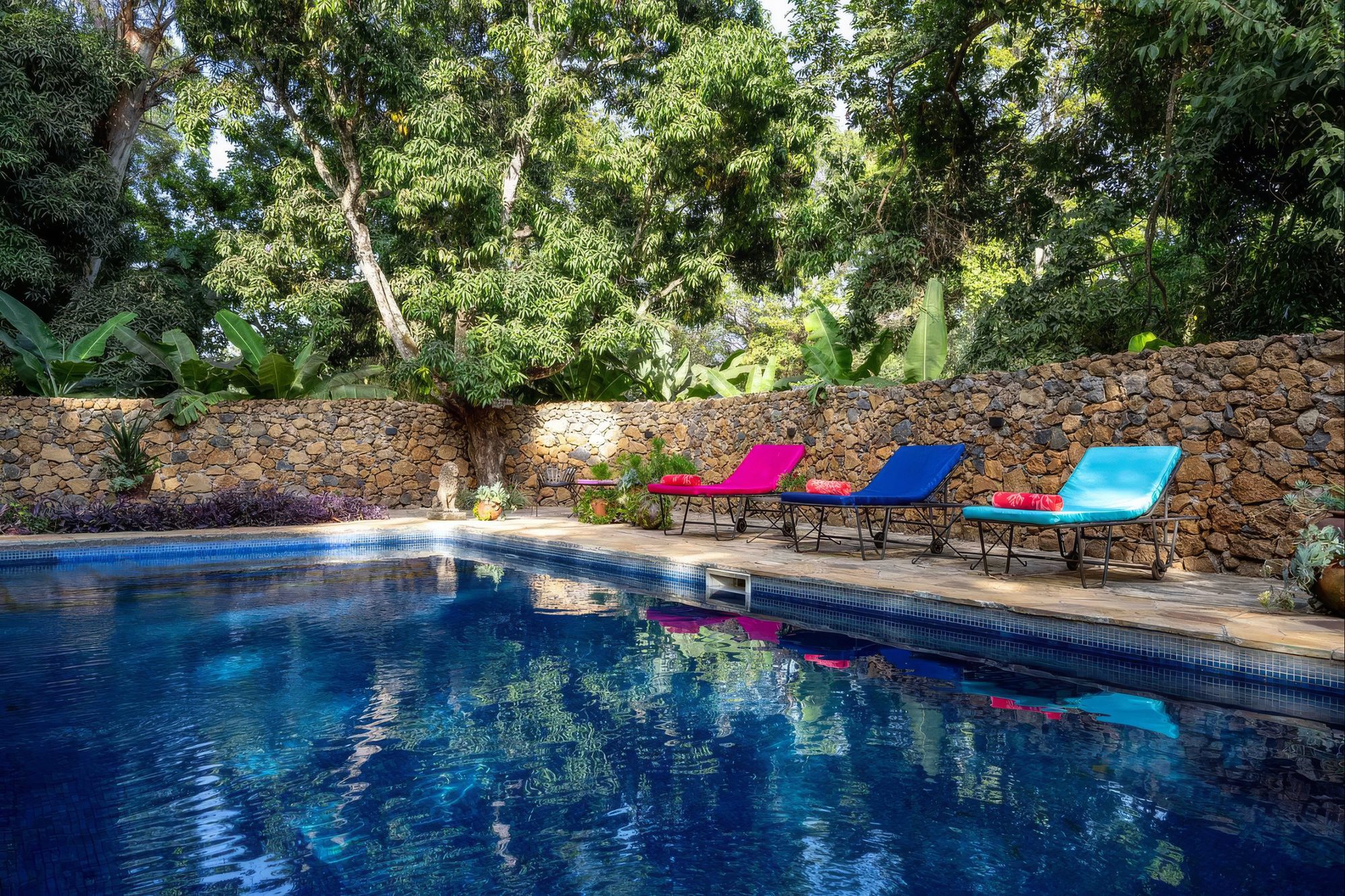 Pool der Mount Meru Game Lodge mit bunten Liegen zwischen Bäumen