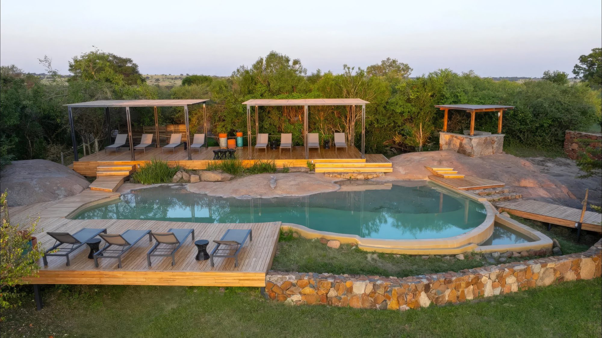 Terraza de la piscina del Sayari Camp Asilia Africa con tumbonas junto a rocas