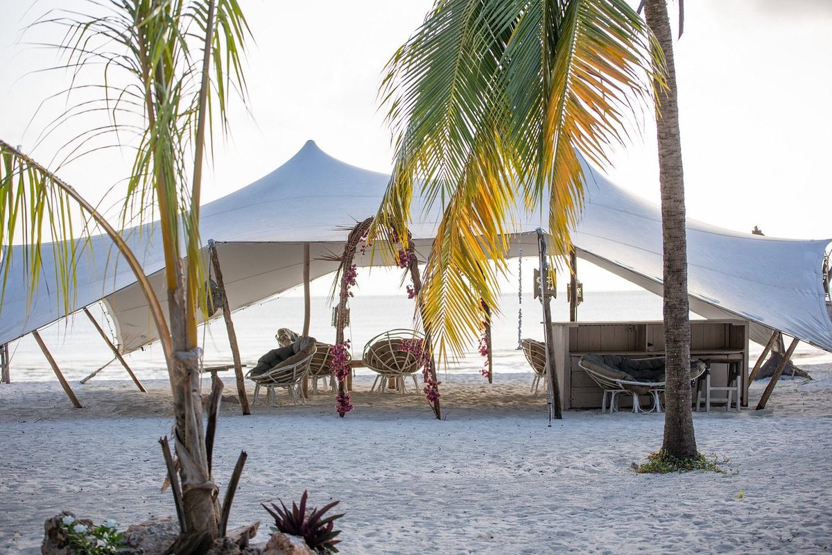 Pabellón de tela entre palmeras directamente en la playa de arena