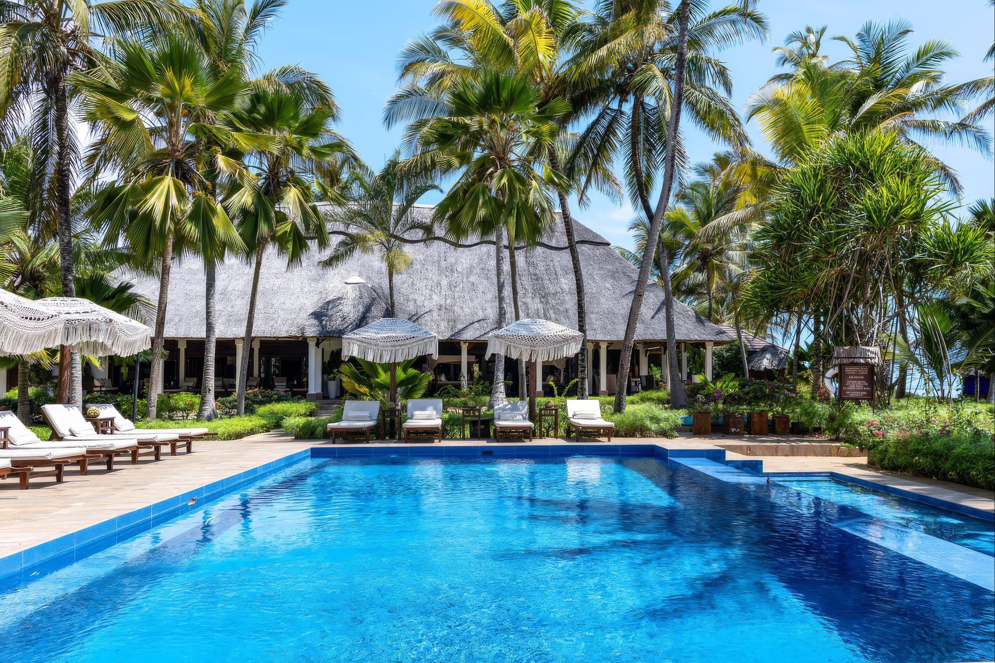 Pool von The Palms Zanzibar zwischen Palmen und Strohdach-Gebäude