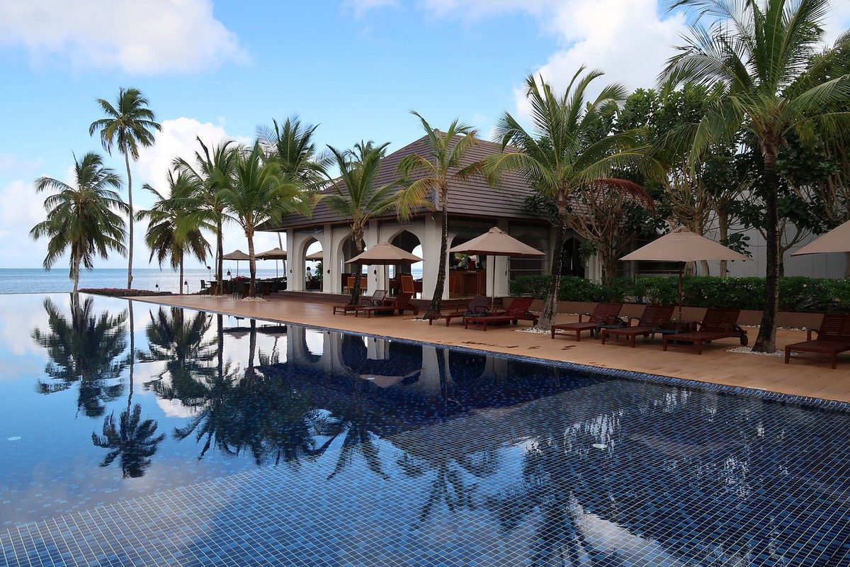 Pool mit Wasserspiegelung, Palmen und Liegen