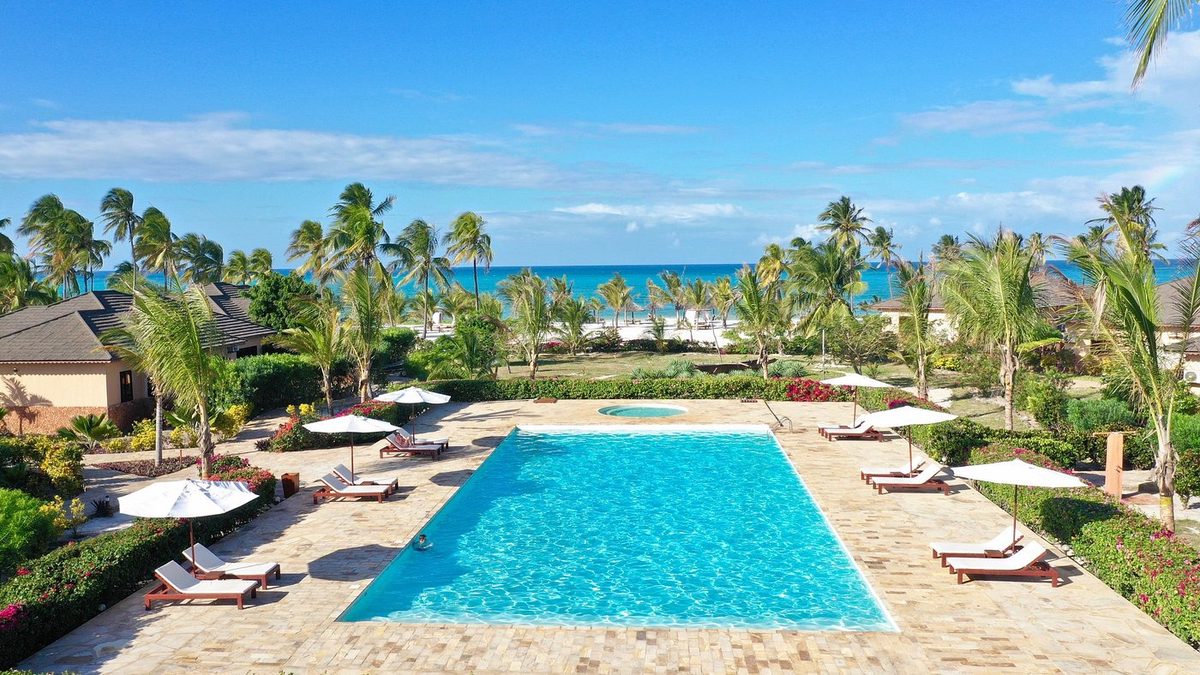 Anlage mit Pool, Palmen und Meer aus der Luft