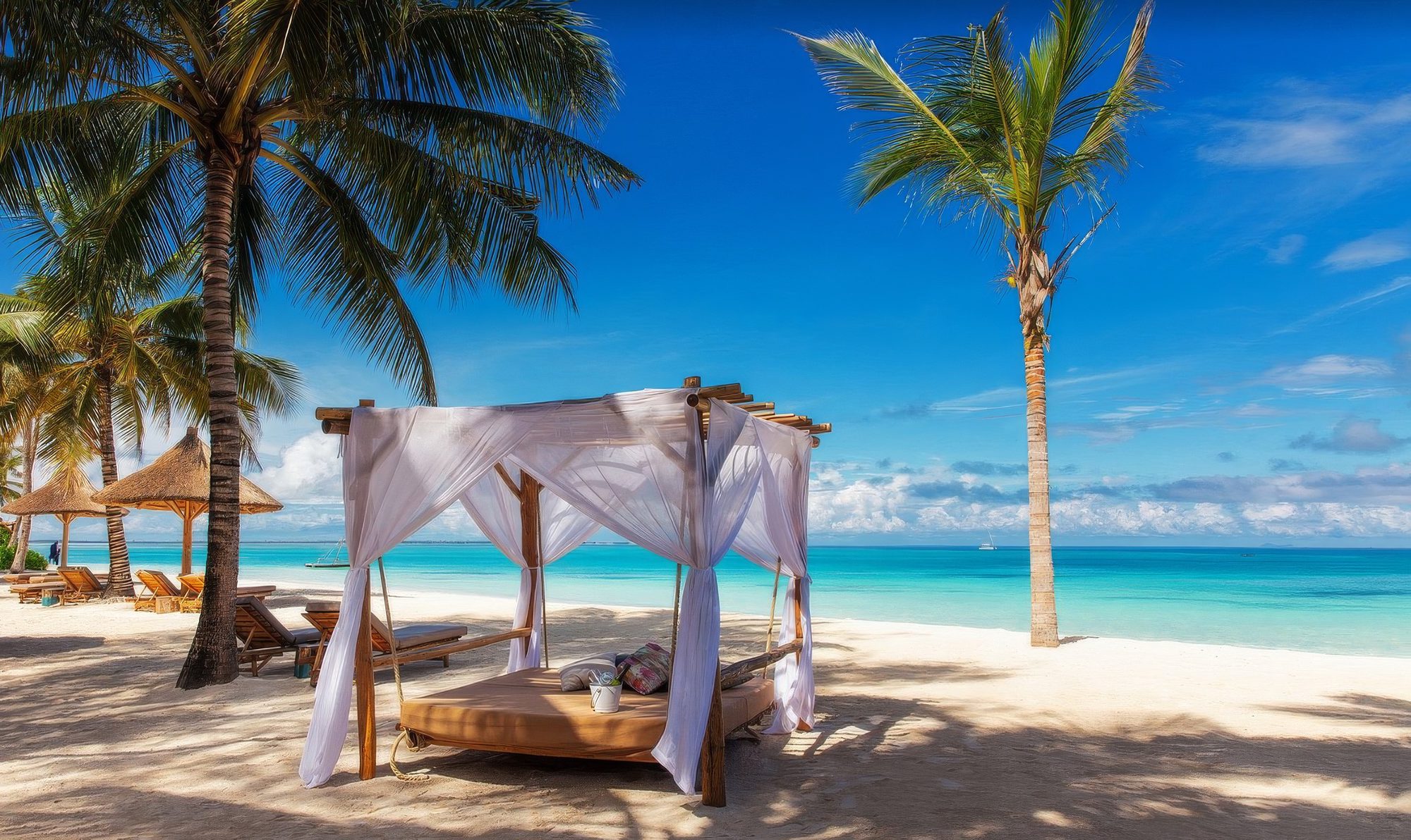Cama con dosel y cortinas blancas en la playa de arena blanca del lodge Zuri Zanzibar frente a un mar turquesa