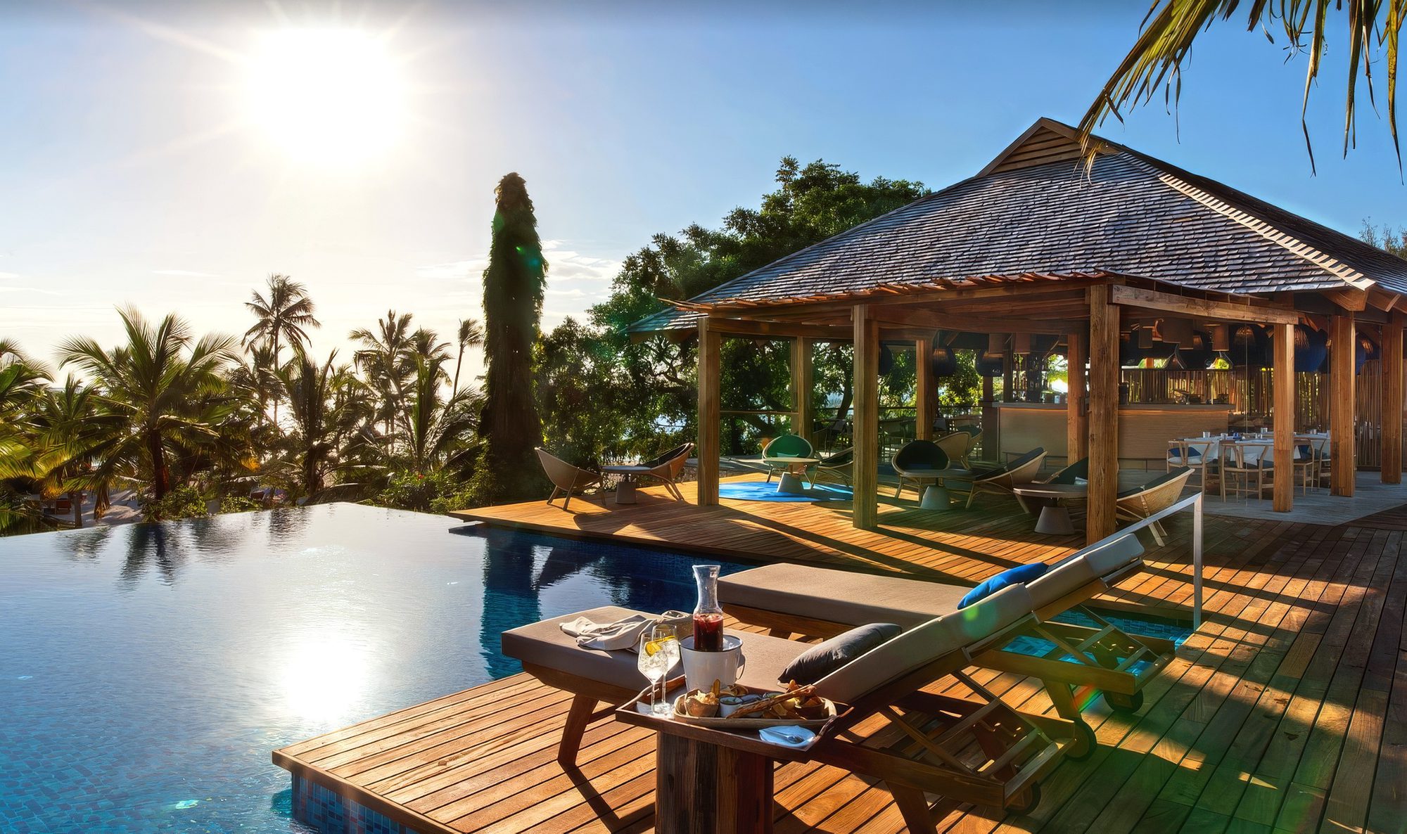 Infinitypool mit Liegen und gedecktem Tisch vor dem offenen Barpavillon der Lodge Zuri Zanzibar