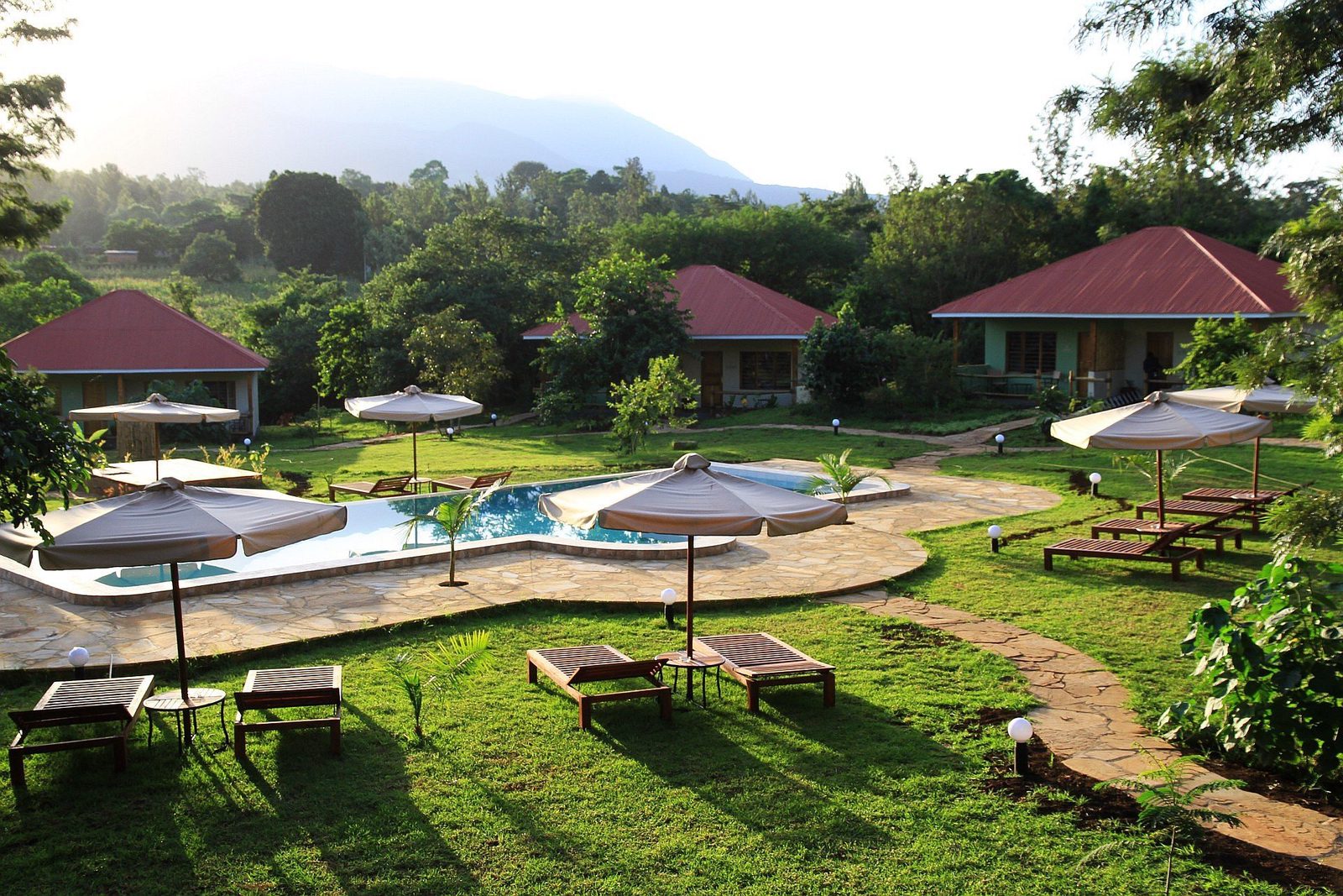 Jardín de la African View Lodge con piscina, sombrillas y tumbonas frente a bungalows con techos rojos