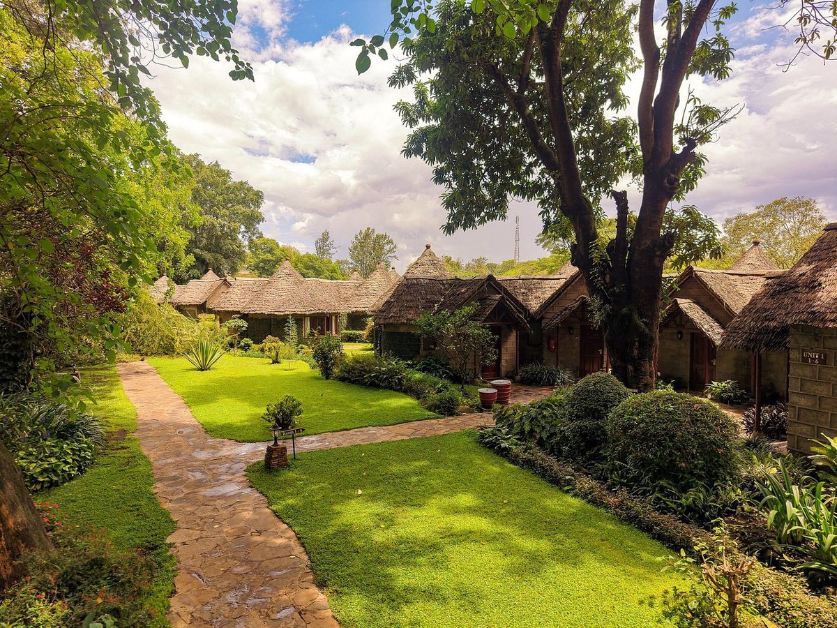 Cabañas con techo de paja del Arusha Serena Hotel Resort & Spa en un jardín verde con sendero de piedra
