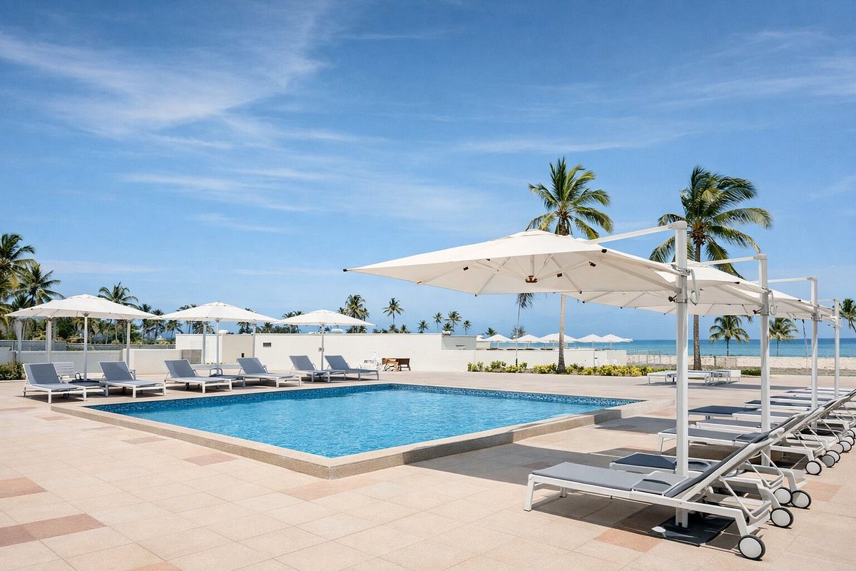 Piscina del Diamonds Bijoux con sombrillas blancas y tumbonas, detrás palmeras y el mar