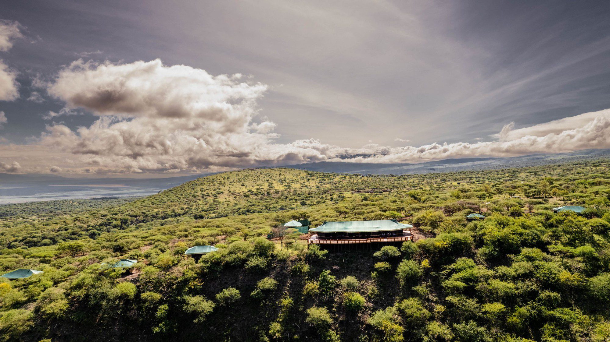Zelte des Embalakai Ngorongoro Camp auf einem bewaldeten Hügel aus der Luft