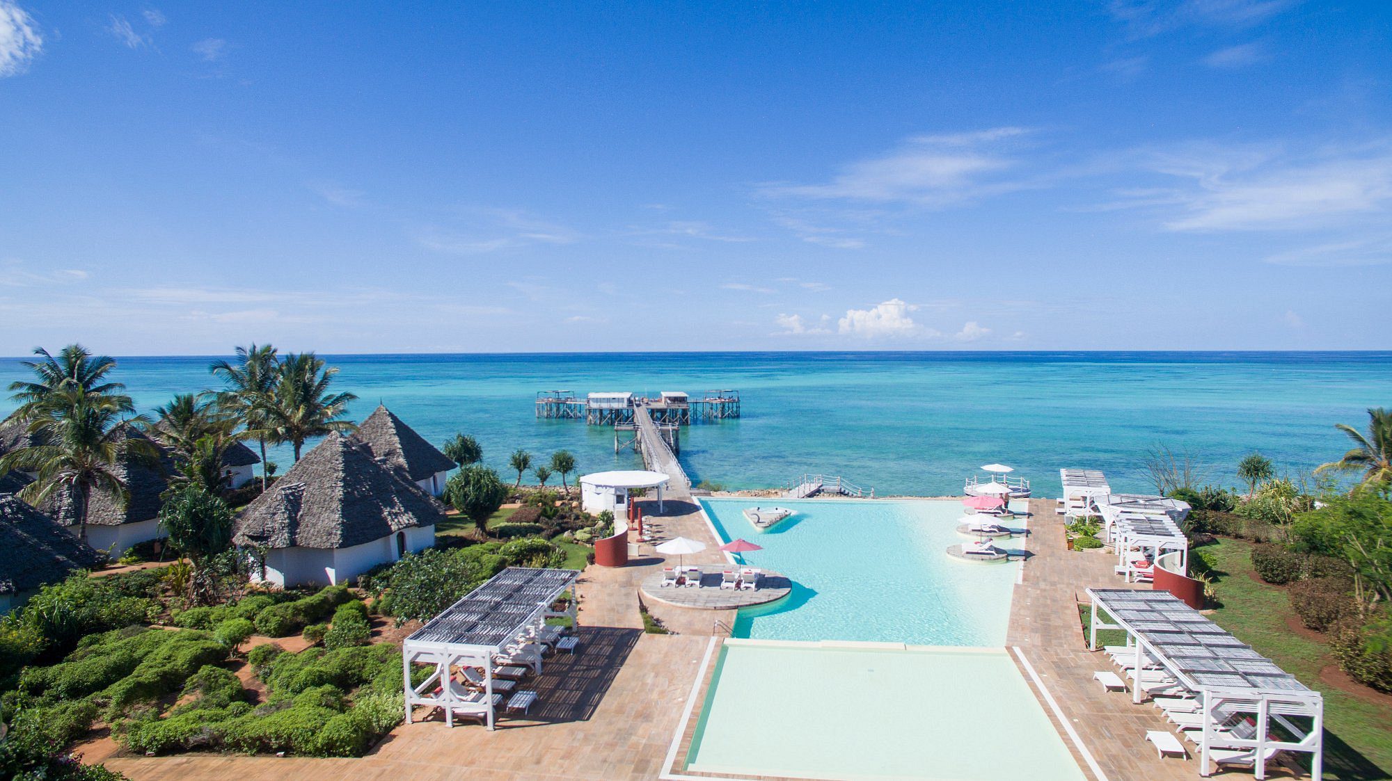 Vista aérea de la piscina del Essque Zalu Zanzibar con pasarela hacia el mar turquesa y villas con techos de paja