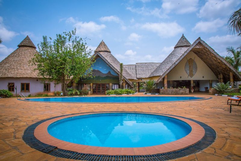 Zwei runde Pools vor dem Haupthaus der Farm of Dreams Lodge mit spitzen Strohdächern