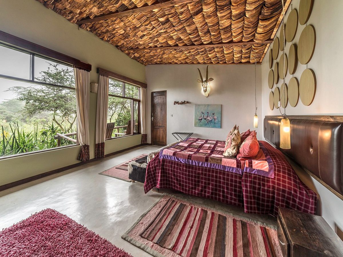 Habitación de la Hatari Lodge con cama doble, manta a cuadros rojos y grandes ventanales al verde