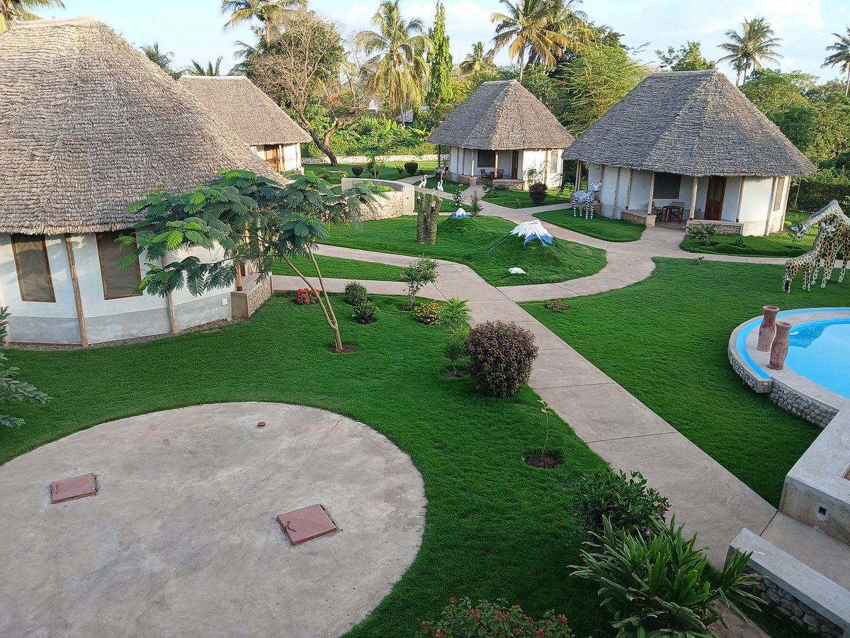 Strohgedeckte Rundhäuser der Ikumbi Lodge in einem Garten mit Pool und Palmen