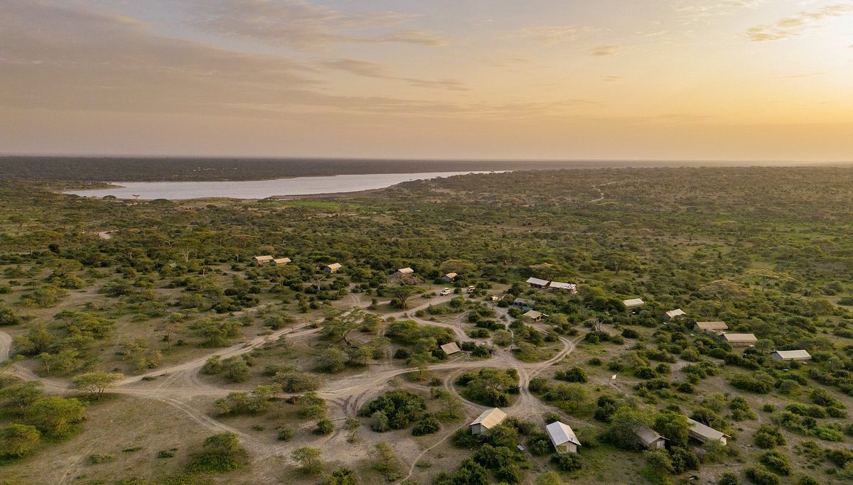 Vista aérea de las tiendas del Intimate Camp Zebra en el matorral, lago en el horizonte al atardecer