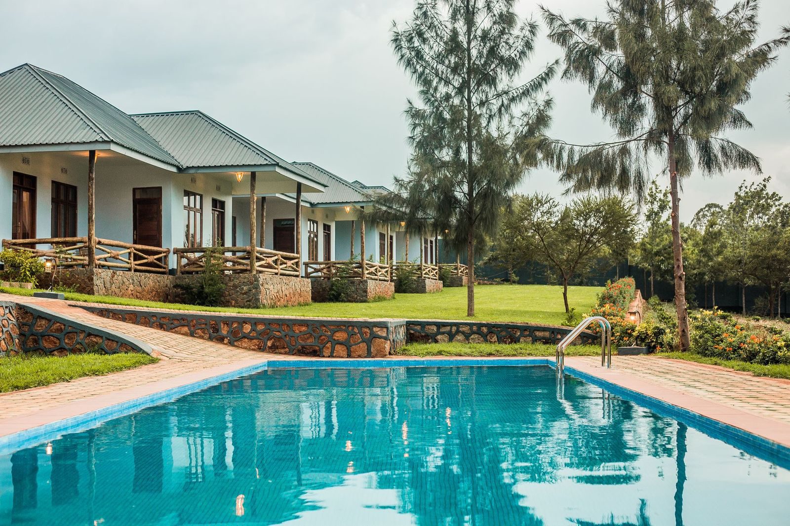 Pool der Kankari Lodge vor einer Reihe Bungalows mit Holzveranden und Rasen