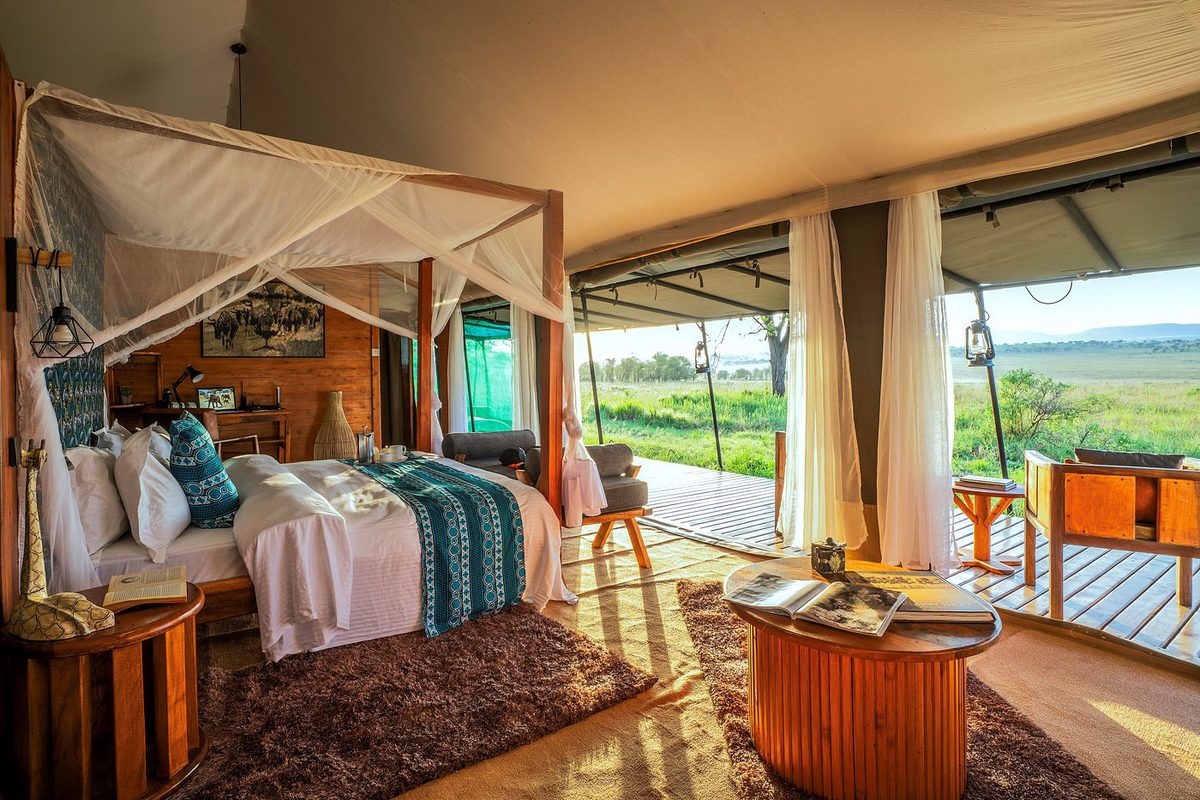 Habitación de la tienda en el Kaskaz Mara Camp con cama con dosel, frente abierta a la terraza de madera y vistas a la pradera
