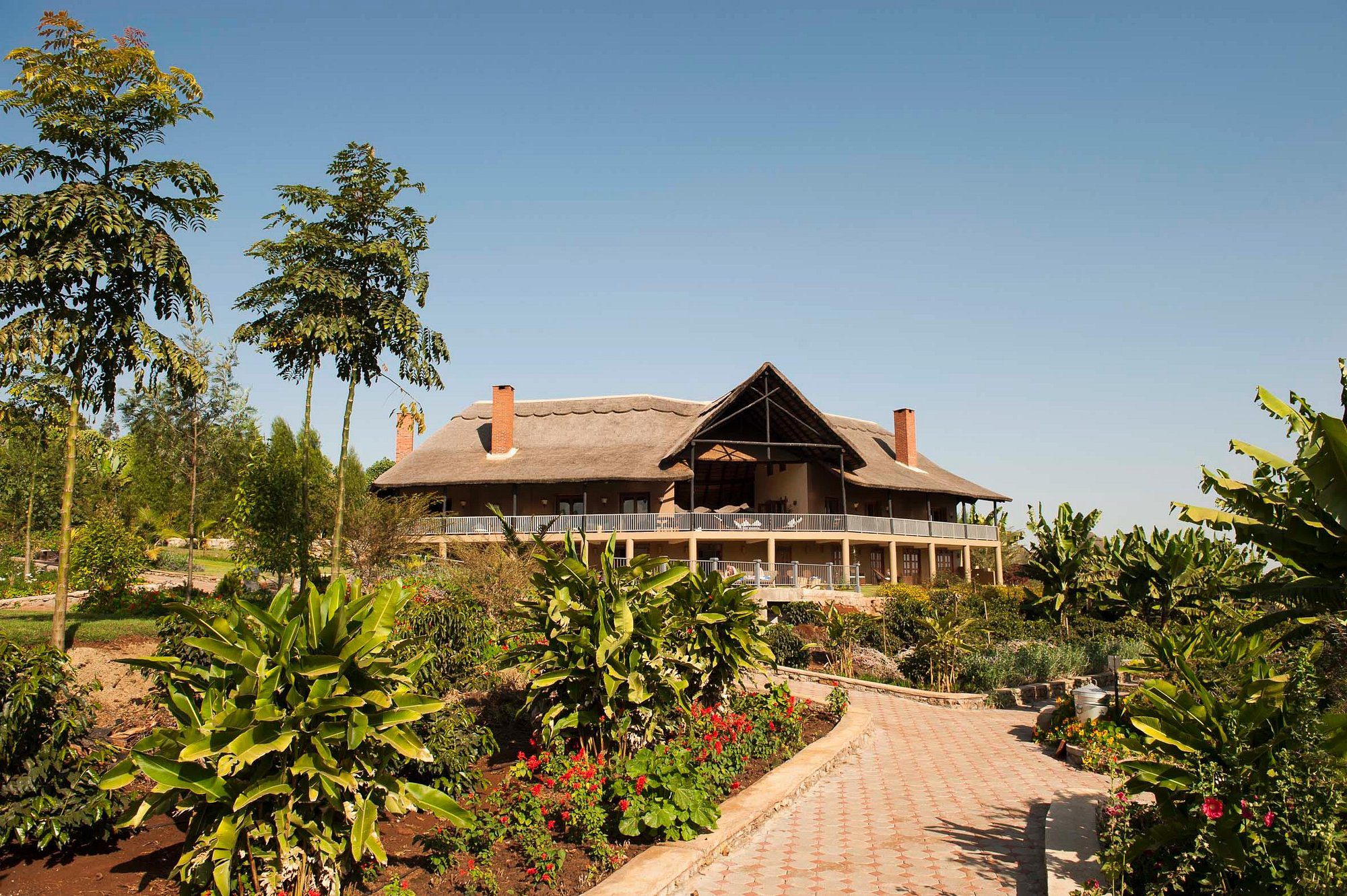 Haupthaus der Kitela Lodge mit Strohdach und Schornsteinen, davor Garten mit Weg und Pflanzen