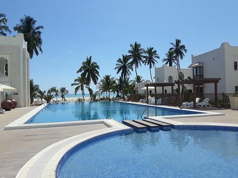 Piscina del LUX* Marijani Zanzibar frente a edificios blancos con palmeras, detrás la playa