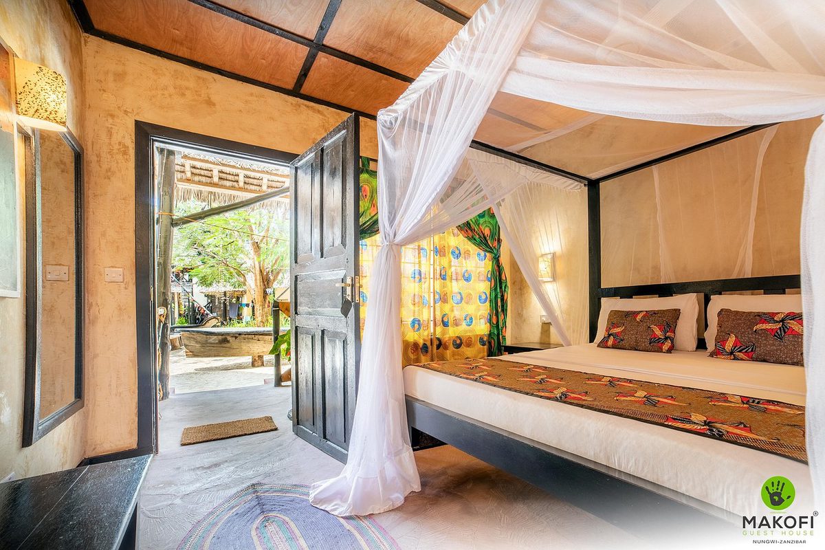 Habitación en el Makofi Zanzibar con cama con dosel bajo mosquitera y puerta abierta al jardín
