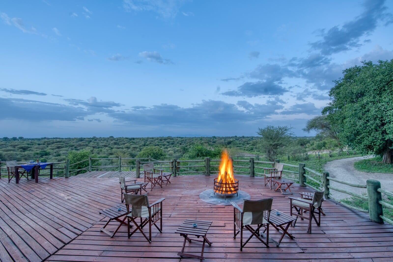 Terraza de madera del Mbali Mbali Tarangire River Camp con hoguera y sillas sobre el matorral