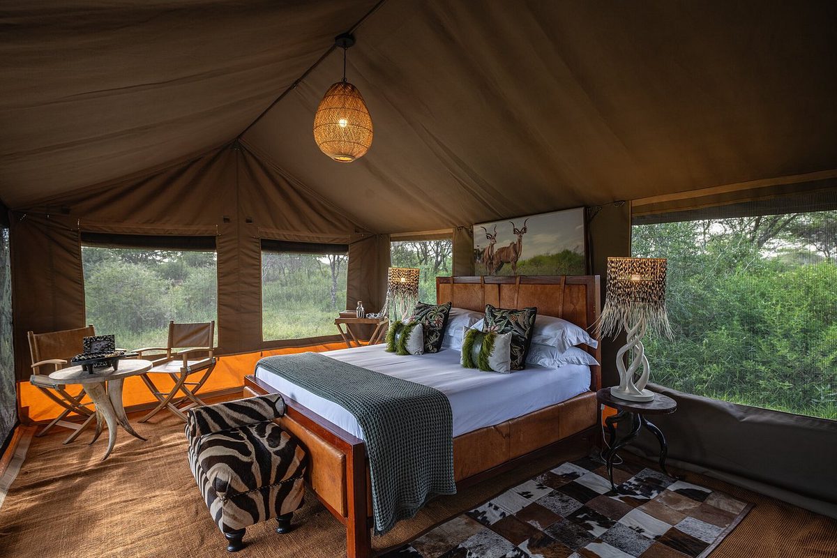 Habitación de la tienda en el Nyumbu Luxury Collection - Mara Camp con cama doble, taburete de piel de cebra y ventanas a la vegetación