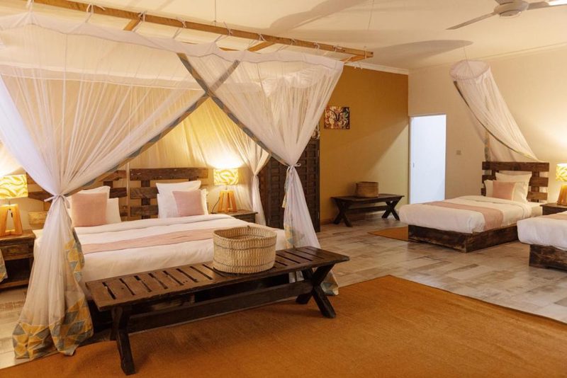 Habitación de la Olerai Lodge con cama con dosel bajo mosquitera, banco de madera y dos camas individuales