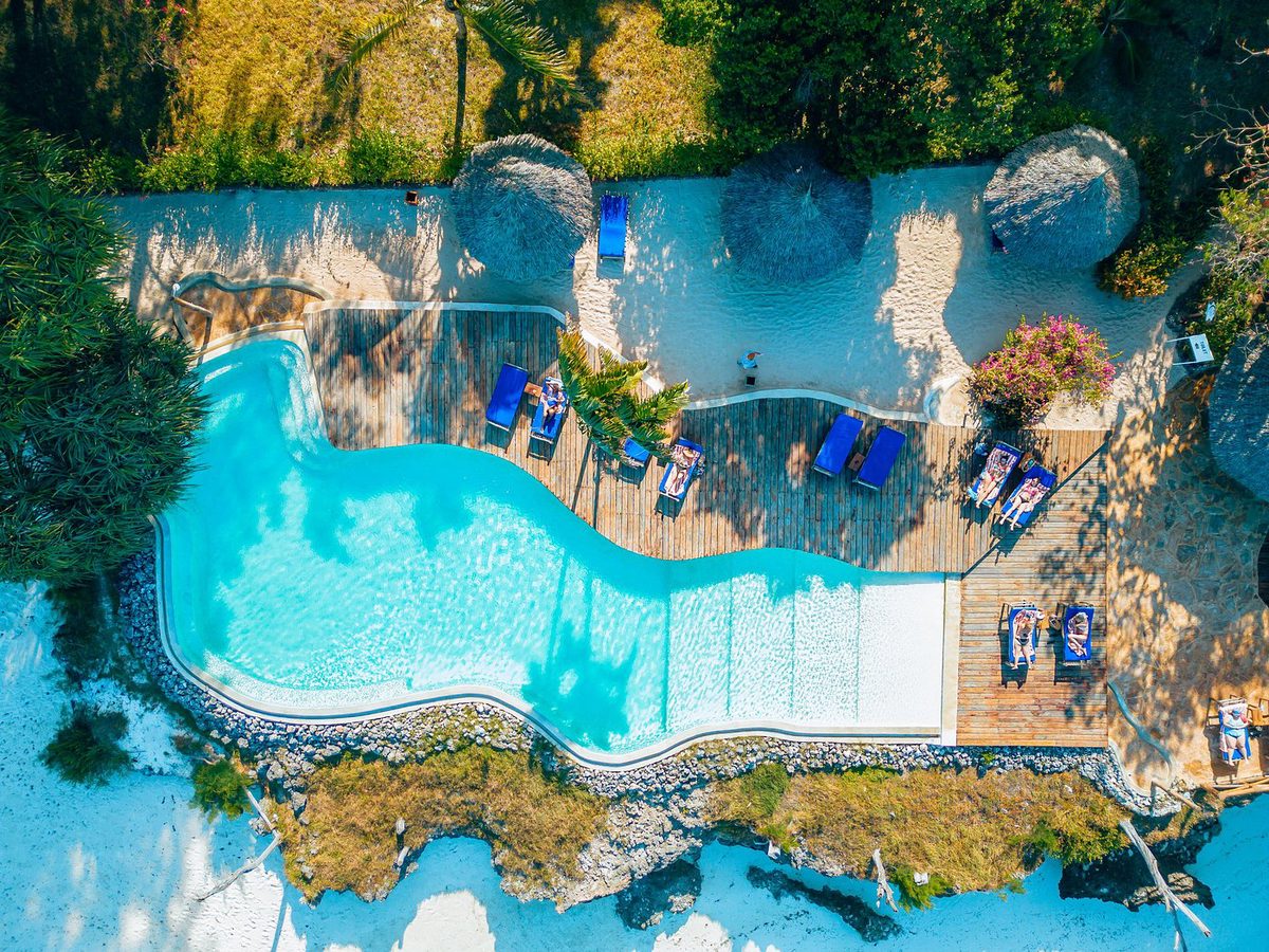 Piscina curva del Pongwe Beach Hotel con terraza de madera y tumbonas en la costa rocosa desde arriba
