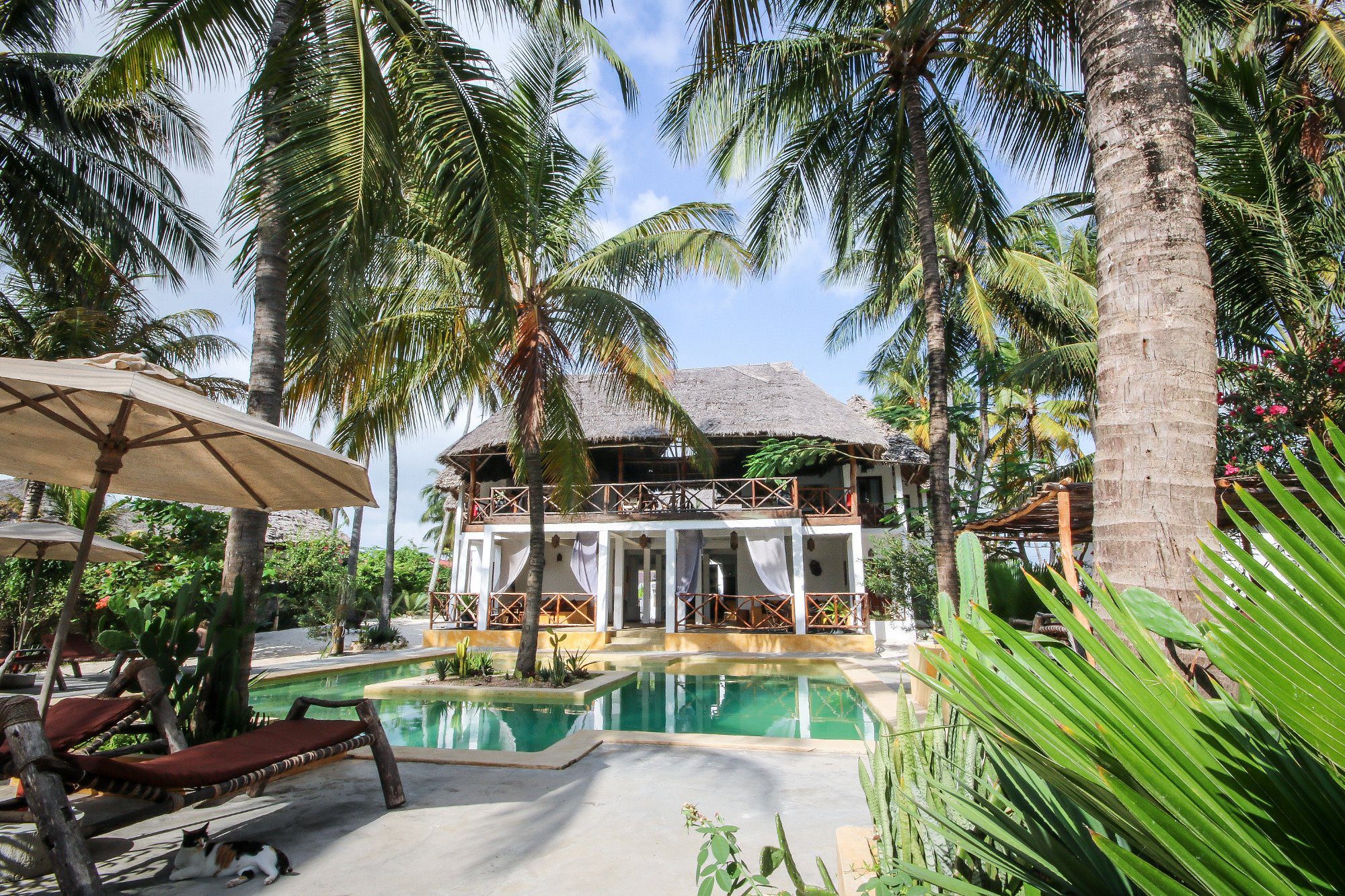 Piscina del Sahari Zanzibar frente a una casa de dos plantas con techo de paja bajo palmeras