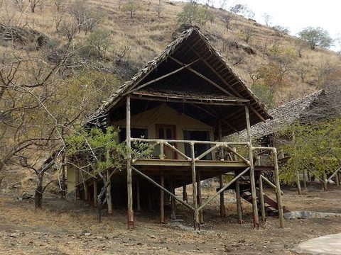 Chalet tienda del Sangaiwe Tented Lodge sobre pilotes de madera con techo de paja, al fondo arbustos y árboles sin hojas