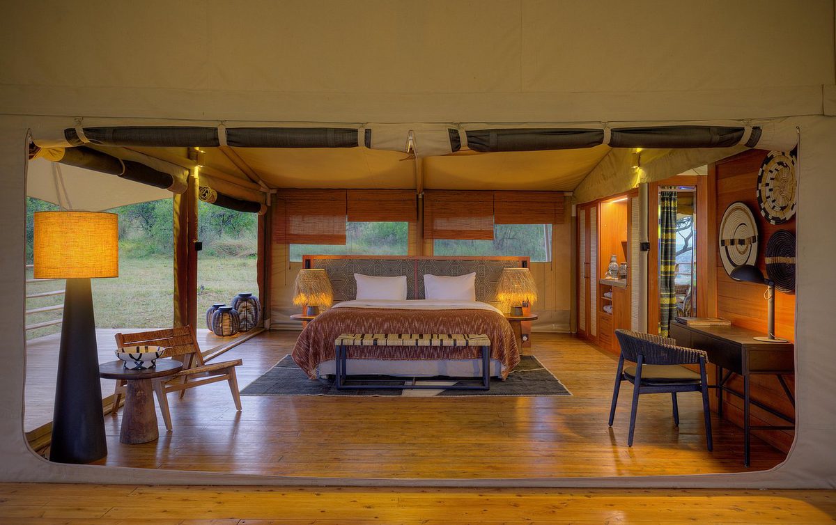 Suite de la tienda en el Serengeti Bushtops Luxury Camp con cama doble, suelo de madera, lámpara de pie y frente abierta