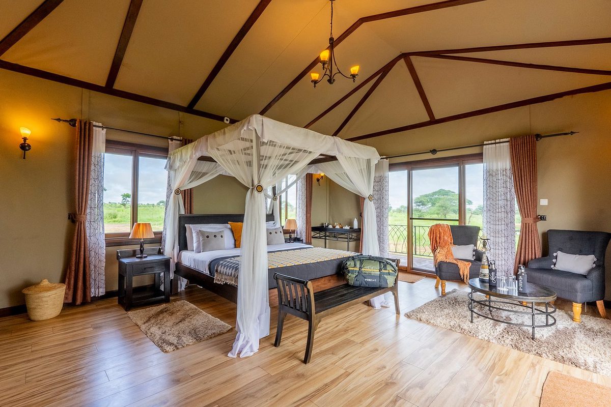 Habitación de la tienda en el Serengeti Sametu Camp con cama con dosel, suelo de madera y zona de estar