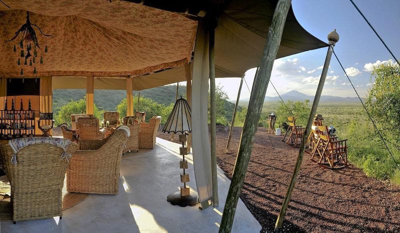 Tienda lounge abierta del Shu'mata Camp con sillones de mimbre y mecedoras, vista sobre la llanura