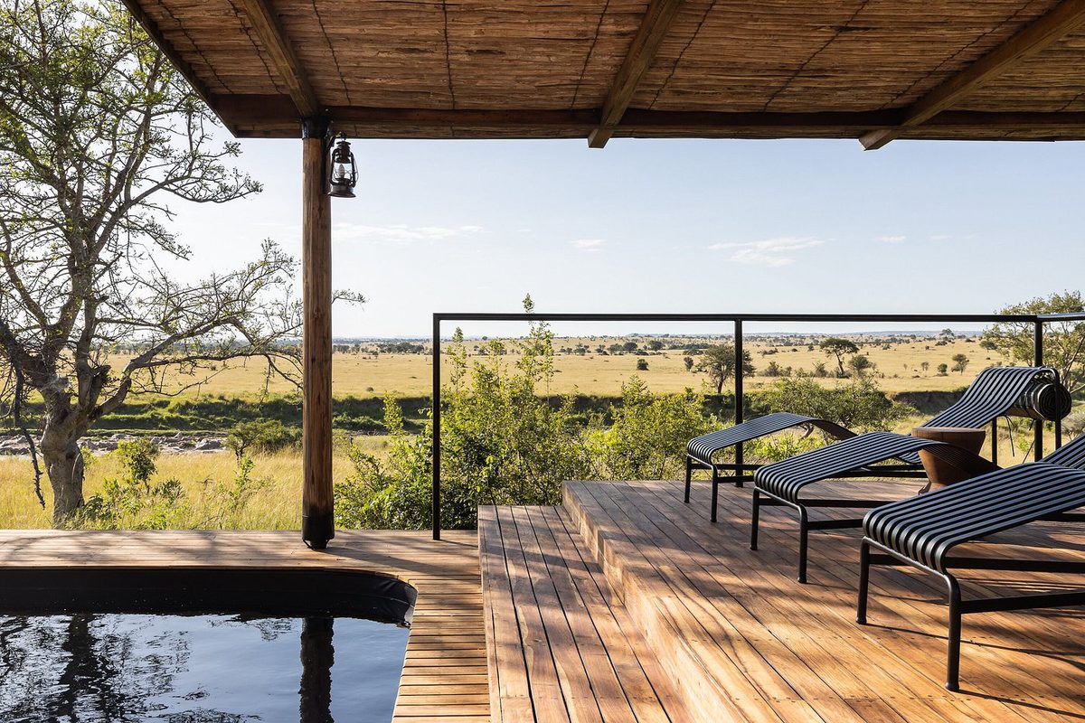 Terraza de madera de Singita Mara River con tumbonas y piscina bajo techo de paja y vistas sobre la sabana