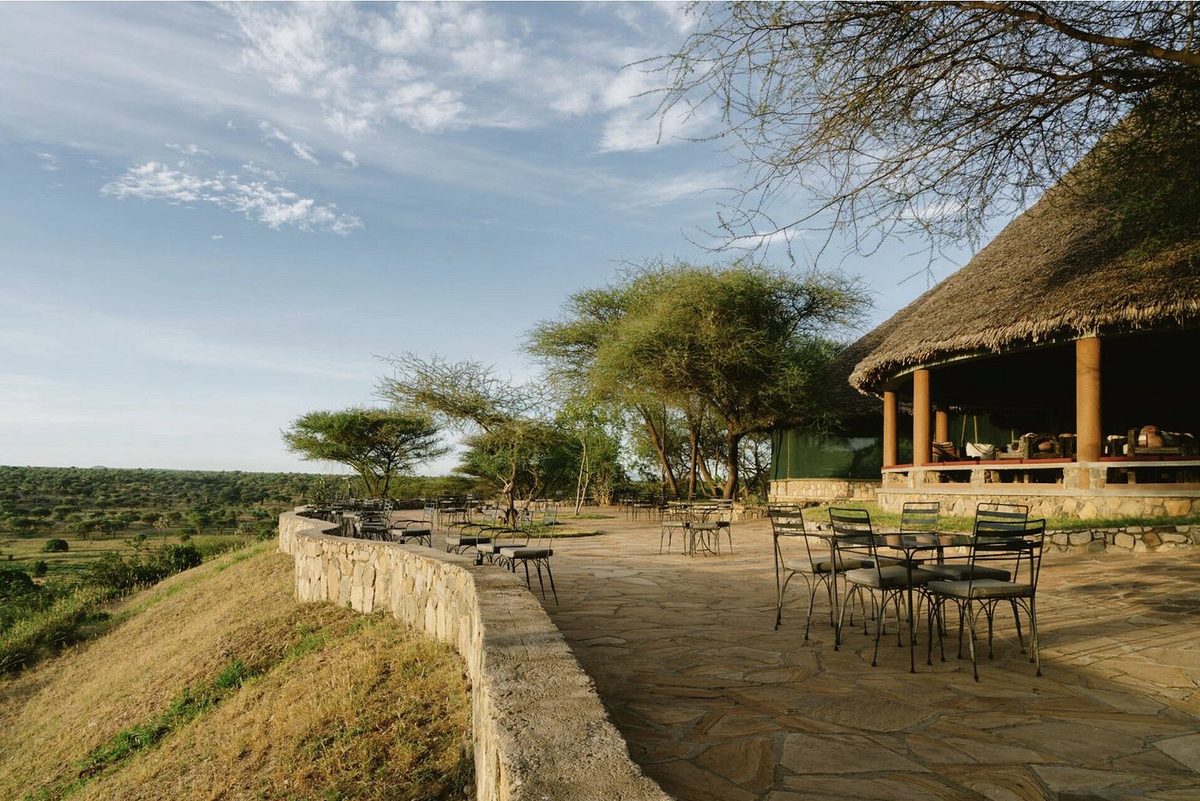 Terraza de piedra del Tarangire Safari Lodge con mesas y sillas y vistas sobre la sabana verde