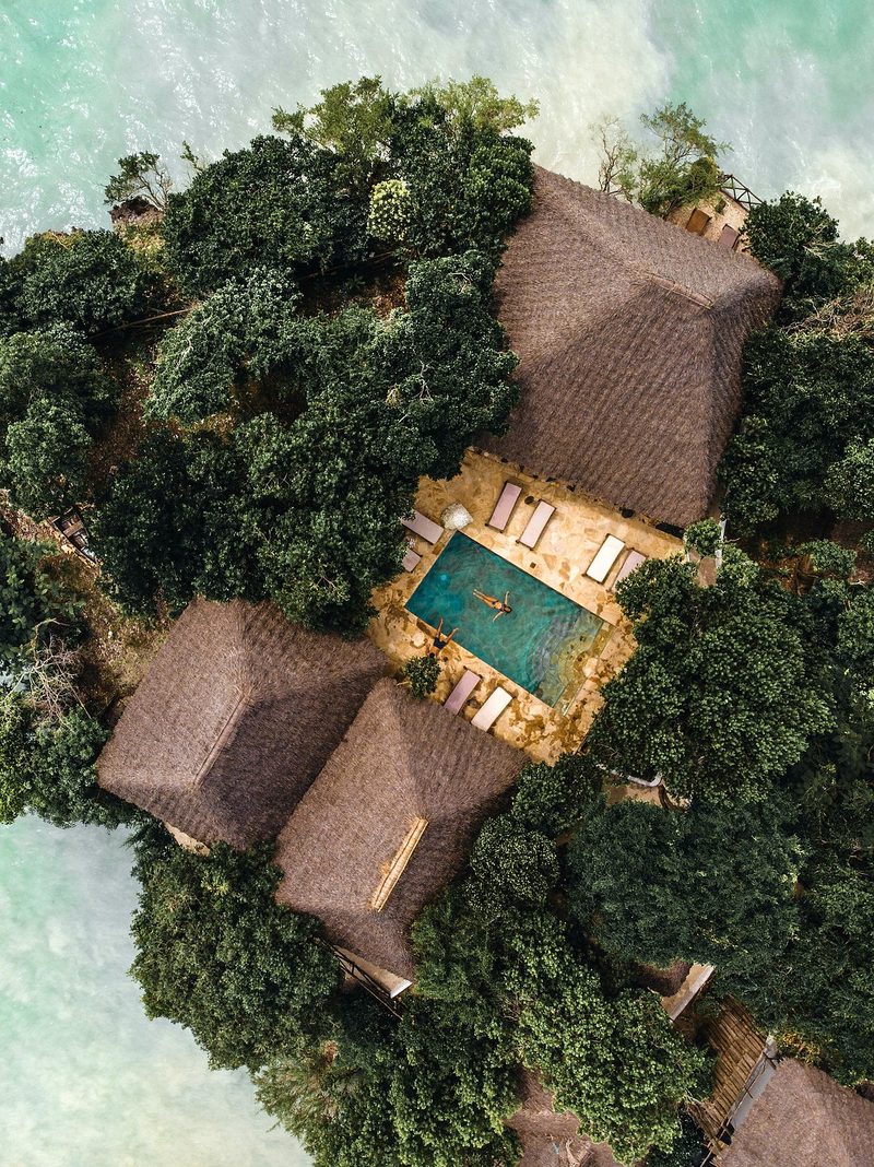 Piscina de The Island - Pongwe Lodge entre casas con techo de paja en una isla rocosa cubierta de vegetación en el mar