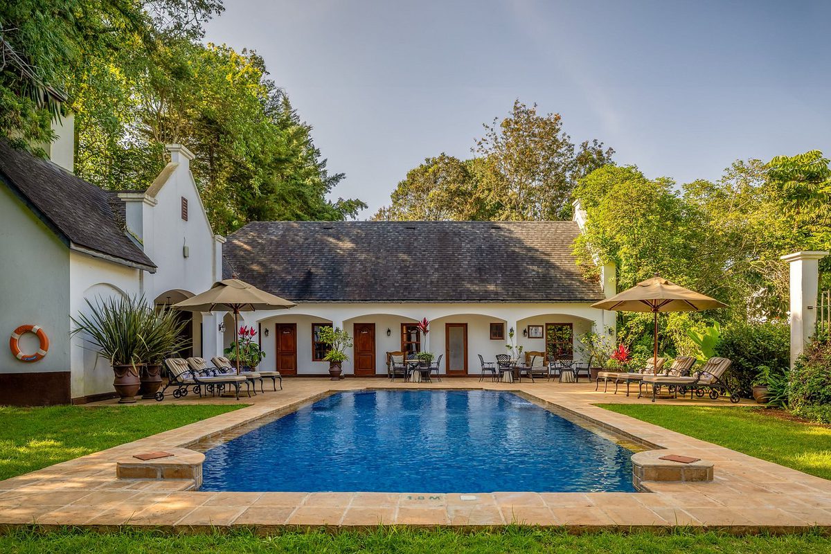 Weißes Herrenhaus von The Manor at Ngorongoro mit langem Pool, Sonnenschirmen und Liegen