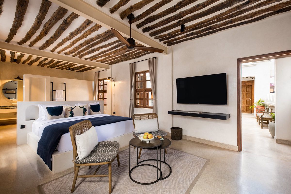 Habitación con techo de vigas de madera, cama doble y zona de estar en el The Neela Boutique Hotel Stone Town