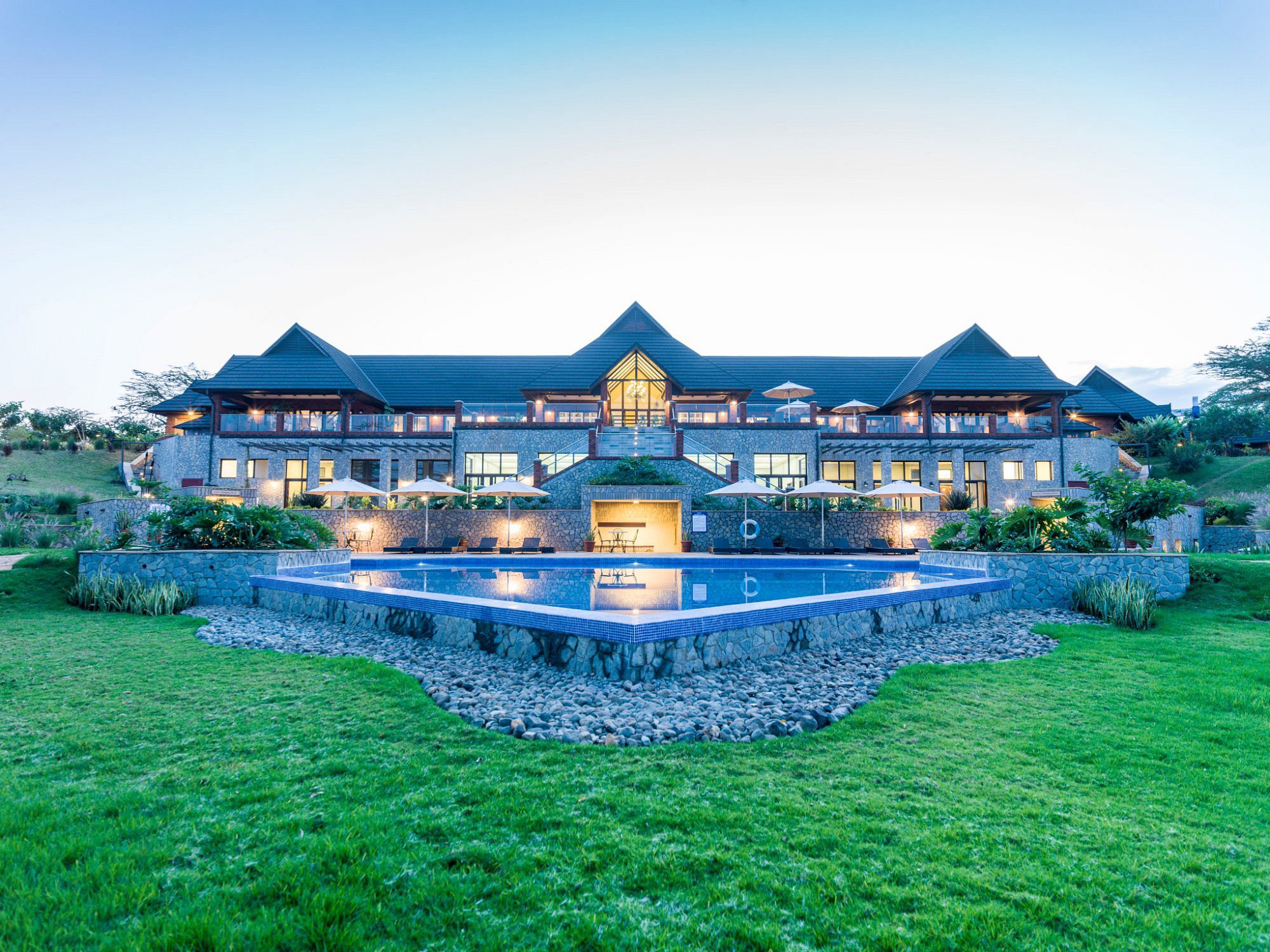 Steingebäude von The Retreat at Ngorongoro mit beleuchtetem Pool und Rasen in der Dämmerung