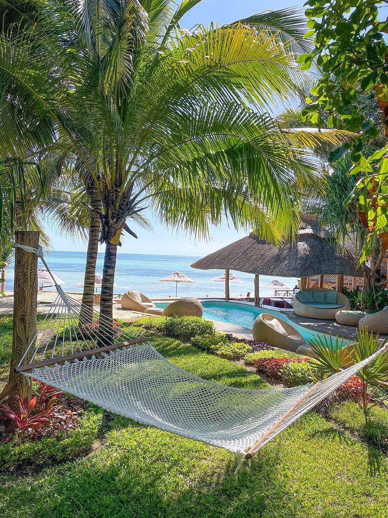 Hamaca bajo palmeras en el jardín del Tulia Zanzibar Unique Beach Resort, detrás piscina y playa