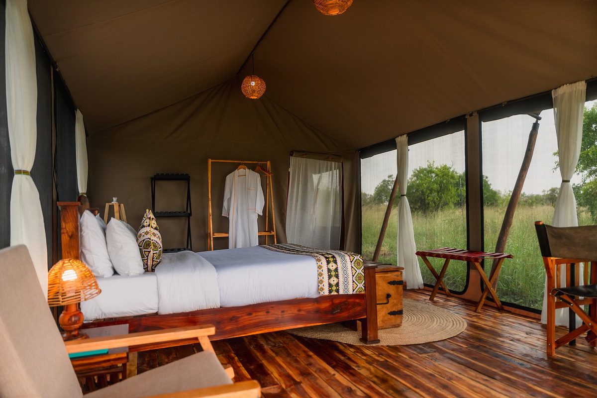 Habitación de la tienda de Untamed Migration Camps con cama de madera, suelo de madera y ventanal hacia la pradera