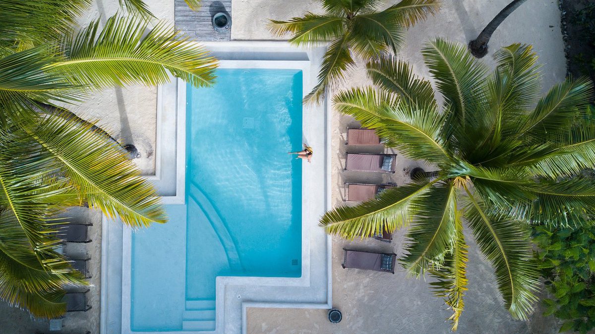 Vista desde arriba de la piscina rectangular del Uzuri Villa Boutique Hotel entre palmeras con tumbonas