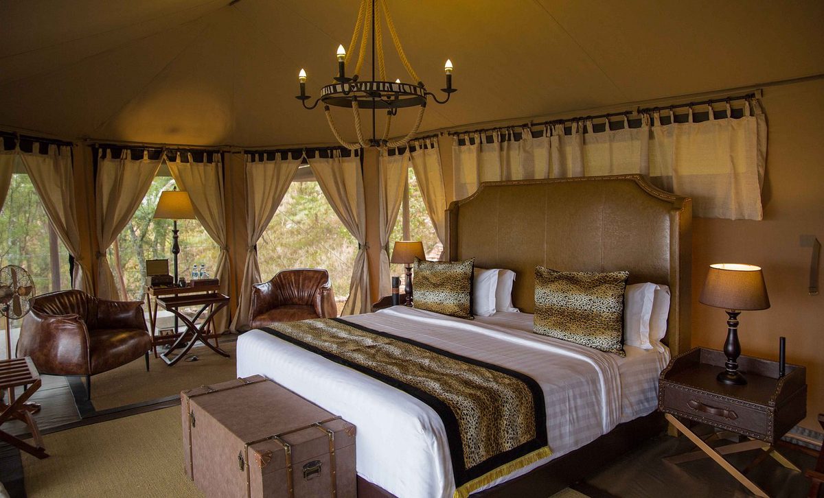 Interior de tienda del Wellworth Ole Serai Luxury Camp - Seronera con lámpara de araña y cama doble con estampado de leopardo