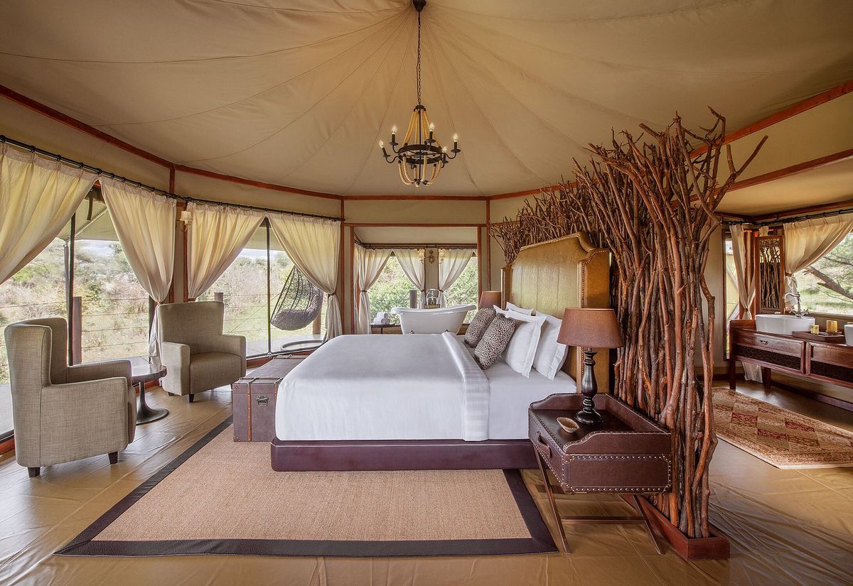 Habitación de la tienda de la Wellworth Tarangire Kuro Treetops Lodge con cama grande, lámpara de araña y cabecero de ramas